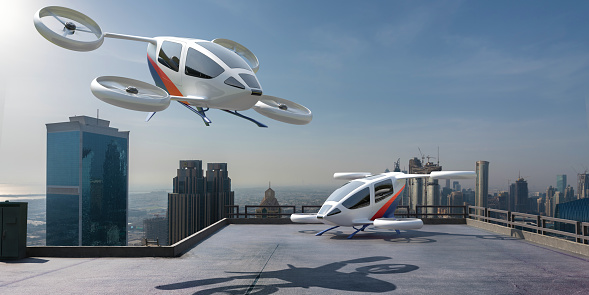 A generic eVTOL aircraft in mid air about to land or take off next to a parked eVTOL on the roof of a skyscraper with other high rise buildings visible in the background. The design of the craft and decals are all generic.