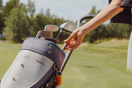Female golf player taking golf club from bag on a summer day.