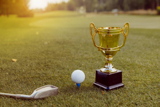 Golden winner cup with golf ball and golf club on green grass on golf course stock photo