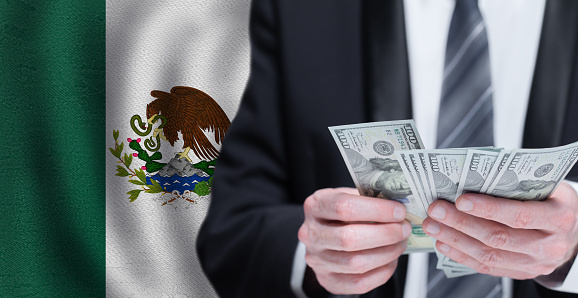 Hands holding dollar money on flag of Mexico
