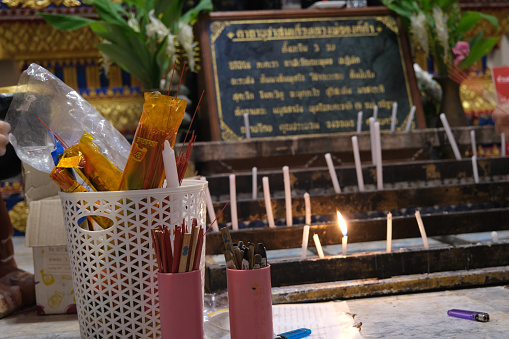 Photo of an altar with votive incense and flower details and candles light for pray in a temple in Thailand