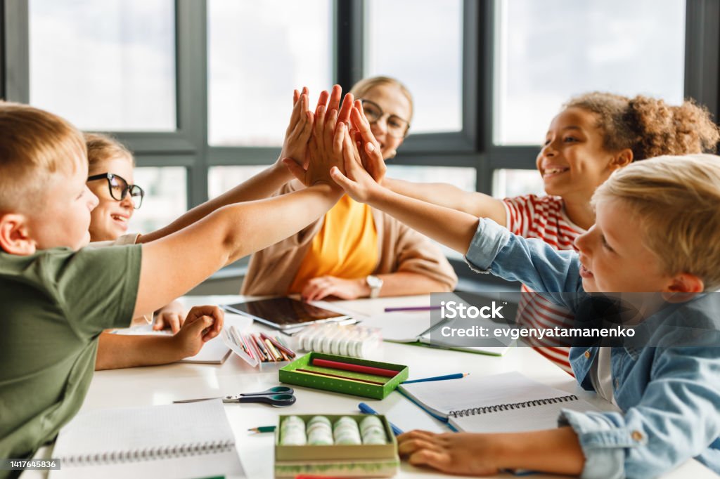 Teacher and joyful students celebrate   successful completion of collective school work in a bright classroom Happy teacher and joyful school kids celebrate together  successful completion of collective school work in a light classroom Student Stock Photo