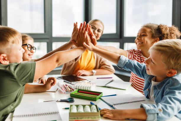 Teacher and joyful students celebrate successful completion of collective school work in a bright classroom Happy teacher and joyful school kids celebrate together successful completion of collective school work in a light classroom schoolboy stock pictures, royalty-free photos & images