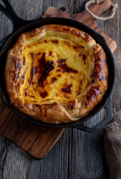 Homemade fresh baked puff pastry tart with cheesecake filling. Served and baked in a rustic cast iron pan isolated on dark wooden table background with copy space. Top view