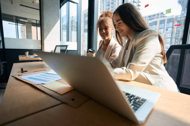istock Smiling women sit at table and watching phone in office 1417648860