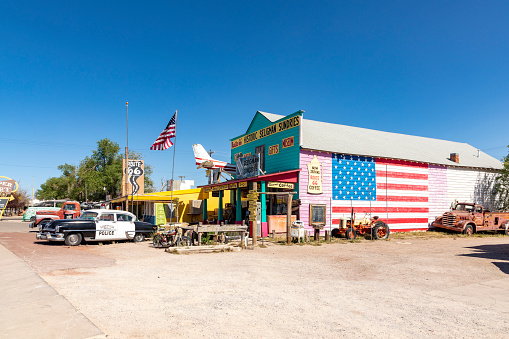 Seligman, USA - May 25, 2022: colorful facade of Shop Historic Seligman Sundries with stars and stripes and an aircraft crashed in the facade and vintage car at route 66 in Seligman, USA.