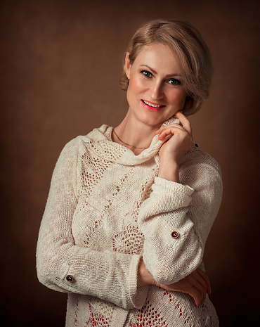A woman in a warm knitted sweater looks at the camera and admires. Handmade, knitting. Blond woman
