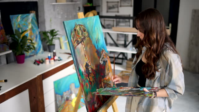 Female artist at work painting on canvas in art studio
