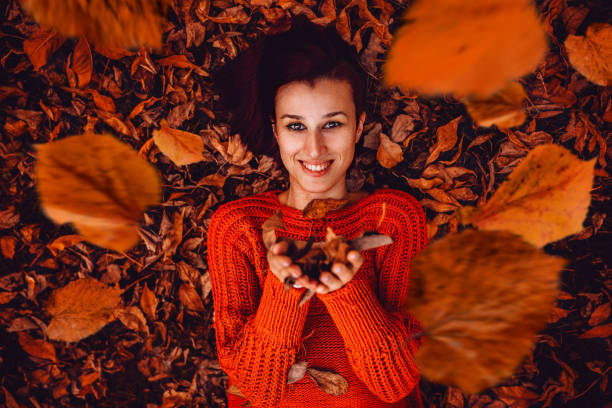 Beautiful young woman lying on autumn leaves in park and smiling.