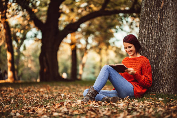 istock Young Woman Leaning On Tree And Reading A Book 1417650216