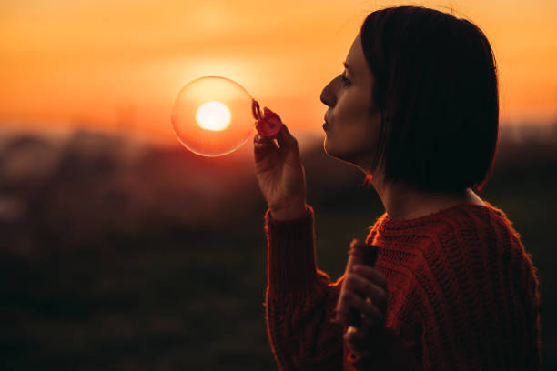 Beautiful young woman blowing bubbles in the park at sunset.