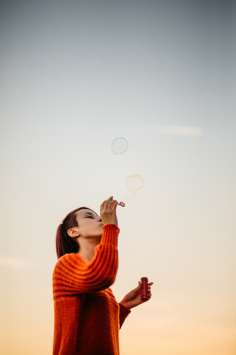Beautiful young woman blowing bubbles in the park at sunset.