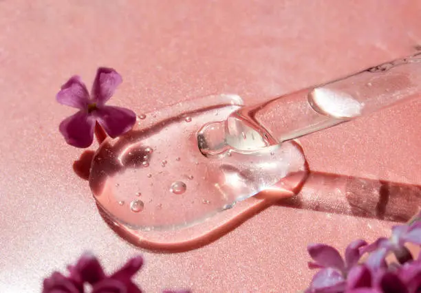 Closeup of pipette with serum, oil, gel with lilac flowers on pink background. Skin care, natural beauty products presentation concept. Macro. Romantic floral composition. Front view, high angle shot