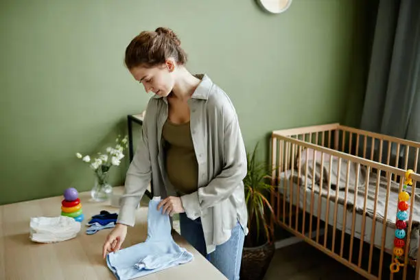 Young pregnant woman preparing things for her baby standing in the kid room