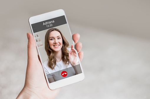 A female hand holds a mobile phone with a girl on the screen, video chat. A woman makes a video call to her friend. Happy young girl smiles on a phone screen, interface, call buttons