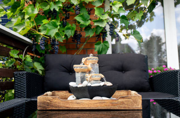 Home patio with black plastic garden furniture, small relaxing electrical zen table fountain on table and real grape vines with grapes hanging on background. Home decor. stock photo