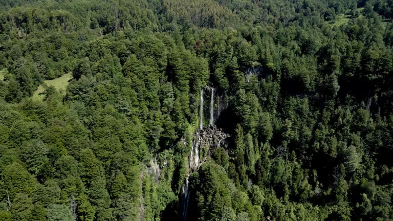 Reverse view of the waterfall la nina encantada hidden in a forest in southern chile - dolly out drone shot