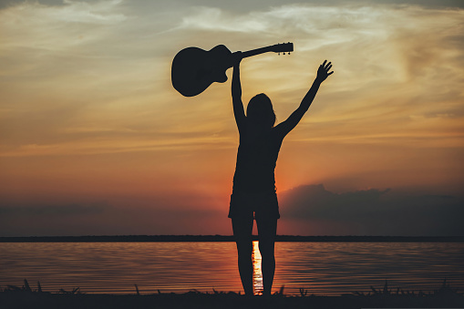 Silhouette woman with guitar in the sunset. Musician holding guitar in hand of silhouette on sunset download photo