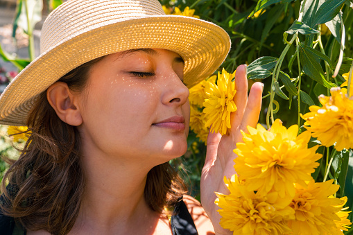 A woman smelling yellow daisies in the garden on a summer day