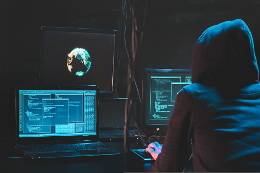 Back hooded hacker using malicious software hack corporate data center. malefactor hidden underground in dark place, multiple displays with phishing code and global map attack. Download photo