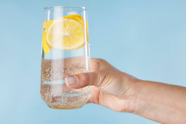 Woman hand holds a glass of homemade cocktail of hard seltzer front on blue background stock photo