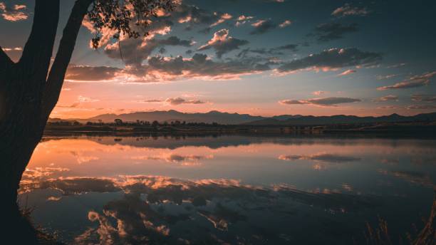 istock Colorful sunset reflected on the water with trees and mountains in the background 1417680807