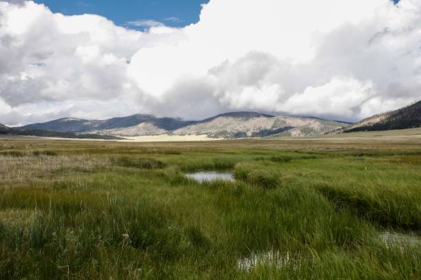 istock Beautiful view of a field with a stream flowing through it with mountains and clouds in background. 1417683733