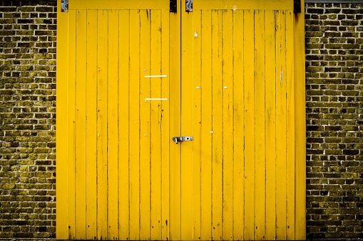 An old wooden yellow door on a brick wall