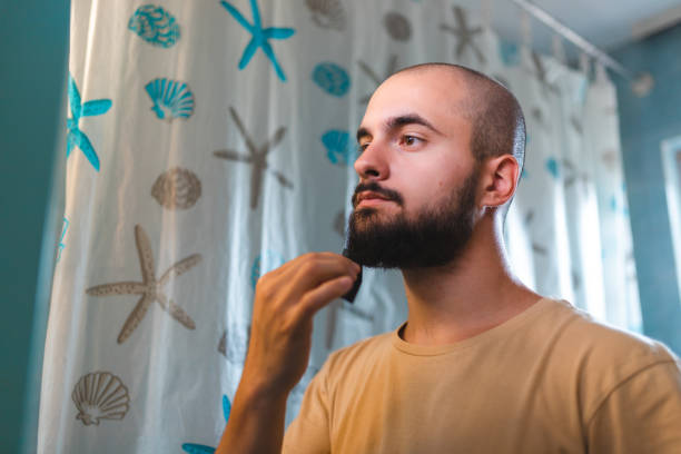 istock Bald young man combing his beard in front of the mirror 1417689381