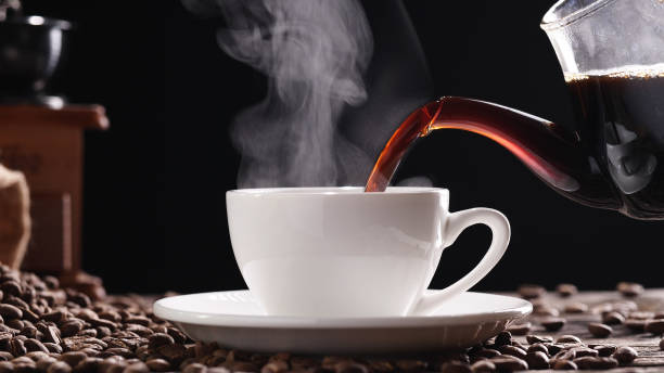 Hot Coffee Cup Concept. Pouring coffee into white coffee cup, mug with classic vintage grinder espresso manual and beans, natural steam smoke on old wood table in morning black backgrounds