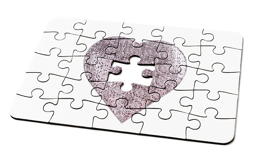 two puzzle pieces patterned with many puzzle pieces of different colors, symbol of the autism awareness, on a white rustic wooden background