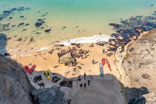 Ballycastle, Northern Ireland. 13 August 2022. People with Kayaks on beach below the Carrick-A-Rede Rope Bridge