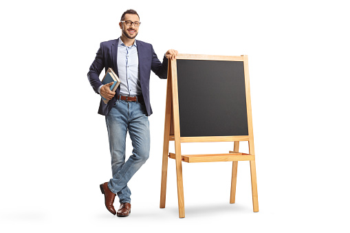 Full length portrait of a male teacher standing next to a blackboard isolated on white background