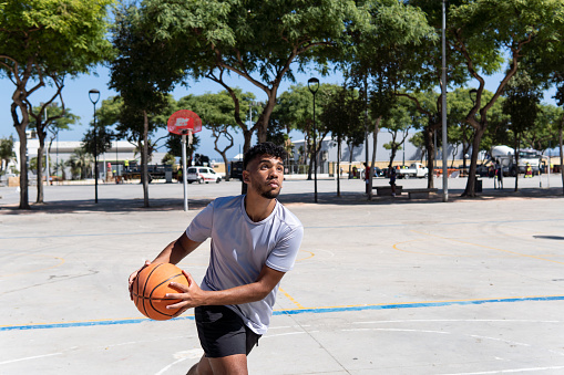 Young muslim man playing street basketball on a city court, training and sport concept