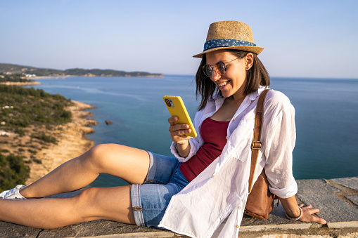 A young woman is using the phone while enjoying the viewpoint at the sea