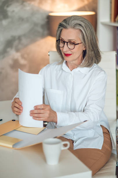istock Gray-haired woman sitting at the table and working with project documentation 1417696005