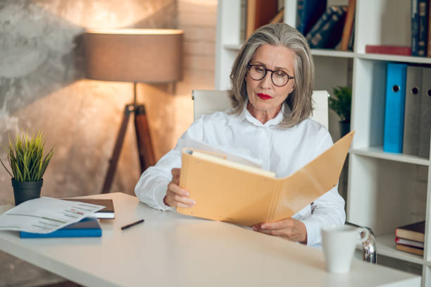 istock Gray-haired woman sitting at the table and working with project documentation 1417696008
