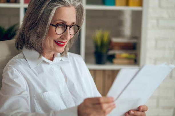 istock Gray-haired woman sitting at the table and working with project documentation 1417696015