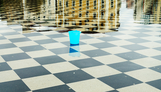 Bucket on a wet checked town square after rain, reflections of houses in the background.