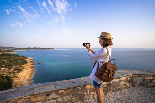 A young woman takes a photo of the view of the sea from the viewpoint with a camera