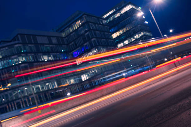 Light trails from vehicles passing by a modern office building at night.