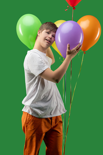 Teen with Down syndrome touching a bunch of inflated bright colorful balloons and looking ahead