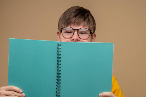 istock Boy in eyeglasses concealing his visage behind the notebook 1417710339