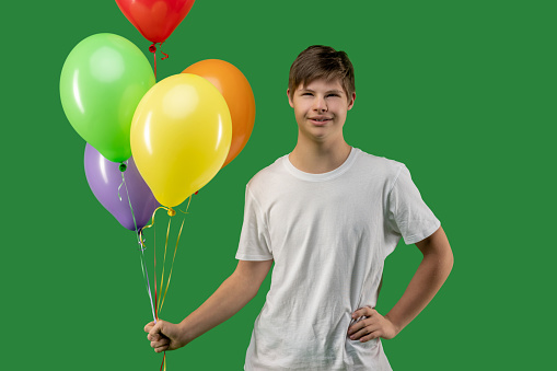 Cute pleased adolescent with Down syndrome holding a bunch of inflated colorful balloons in his hand