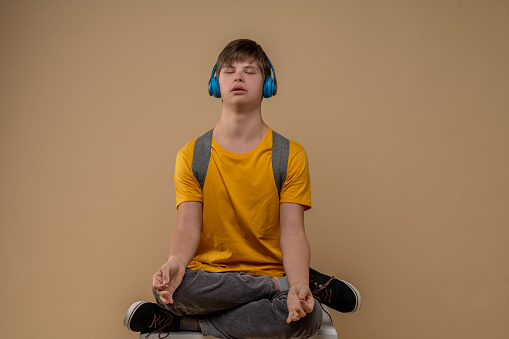 Calm adolescent in the wireless headphones sitting in the half lotus pose with gyan mudra during the meditation session