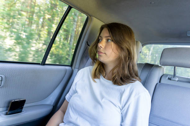 beautiful girl rides in car in the back seat and looks out the window stock photo