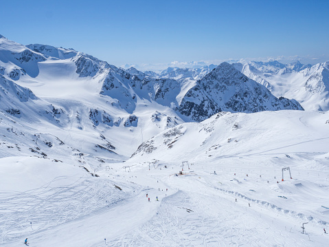Winter landscape with snow covered mountain slopes and pistes with skiers enjoying spring sunny day at ski resort Stubai Gletscher, Stubaital, Tyrol, Austrian Alps.