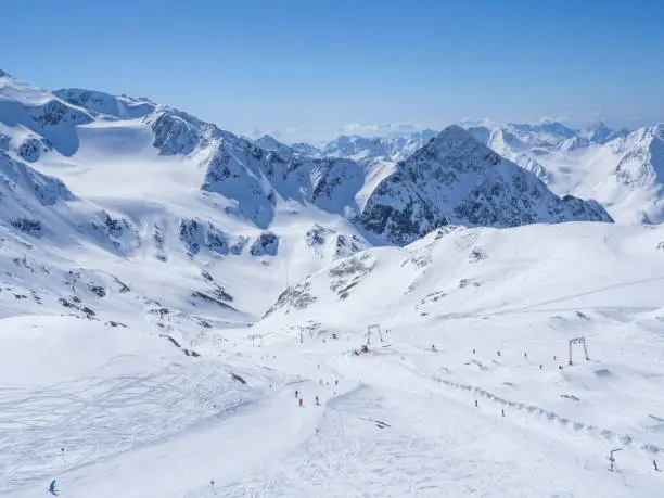 Winter landscape with snow covered mountain slopes and pistes with skiers enjoying spring sunny day at ski resort Stubai Gletscher, Stubaital, Tyrol, Austrian Alps.