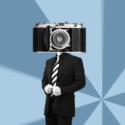 A young businessman in a black business suit headed by huge old vintage retro photo camera standing on a blue graphic background. Trendy collage in magazine style. Contemporary art. Modern design