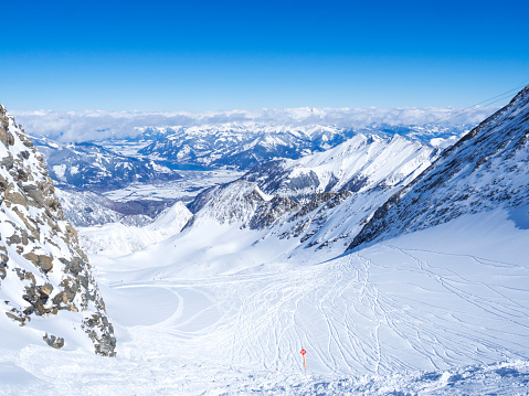 Winter landscape with free ride piste and view on snow covered slopes and blue sky, with Aerial view of Zell am See lake from the top of Kitzsteinhorn mountain on . Kaprun ski resort, National Park Hohe Tauern, Austrian Alps, Europe